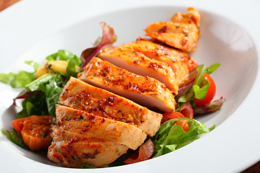 Image of herb roasted chicken breast placed on a bed of fresh salad, both are on a white plate.